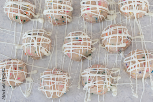 Birthday cake sprinkled edible cookie dough balls with vanilla drizzle on white parchment paper.