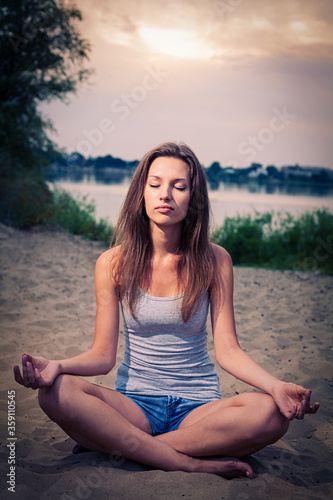 Nice lady is meditating on the sand with her legs crossed and eyes closed