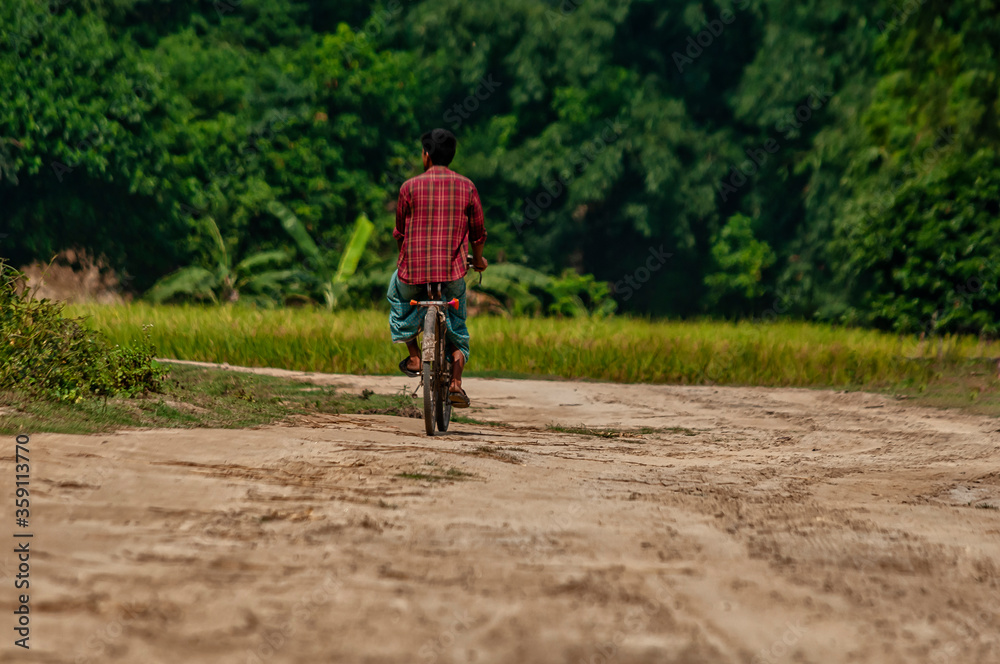 Nayabad village in Kaharole Upazila of Dinajpur District, Bangladesh  – October 08, 2014 – a lone cyclist on the road enjoys the cool weather of winter