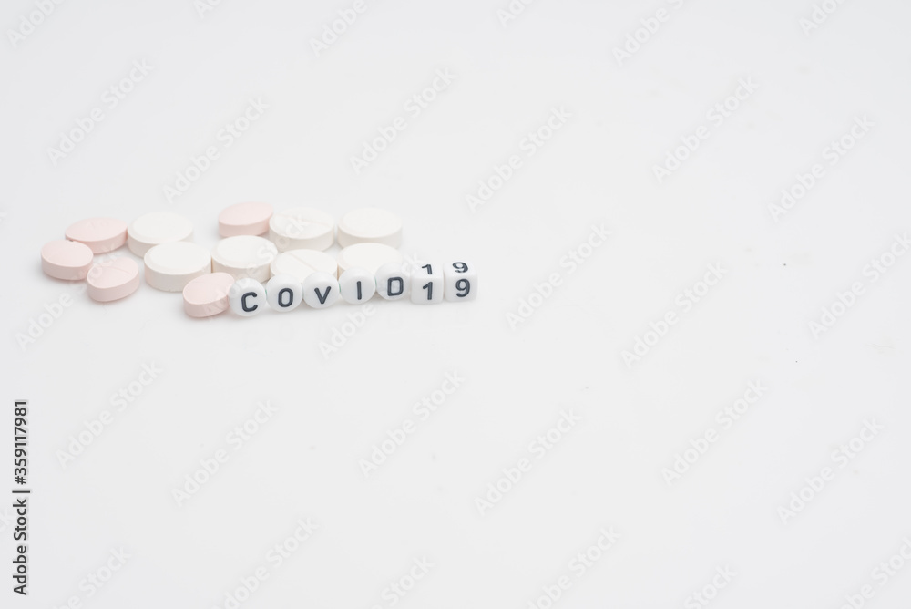 Fototapeta premium The word covid 19 with pills and syringes,over white background and surface