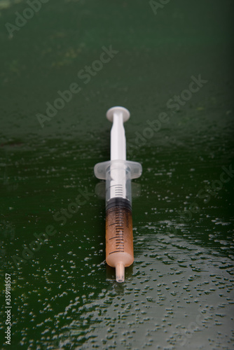 A syringe filled with orange color liquid isolated over green color wooden background