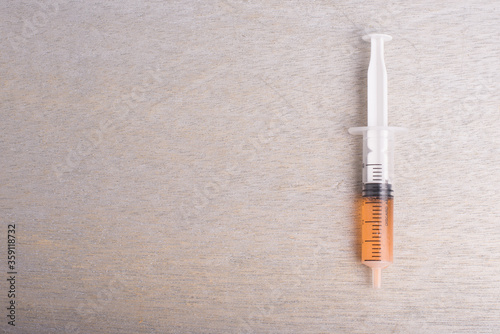A syringe filled with orange color liquid isolated over grey wooden background