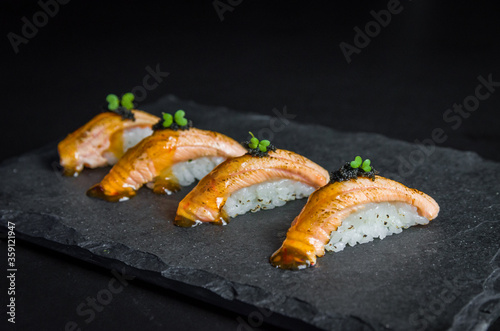 Perfect sushi, traditional Japanese cuisine. Delicious salmon kiguiri with capellin roe (caviar) on the decorated plate, black background.