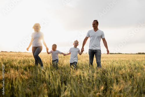 A happy family, dad, mom and two sons walk in a wheat field and watch the sunset. White T-shirts. Harvest cereals.