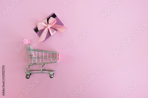Shopping cart and gift card on pink background. Holiday sales, discounts, shopping online concept. Top view, flat lay, copy space