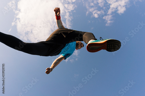 Low angle view of a sportsman who jump and run with blue sky in background
