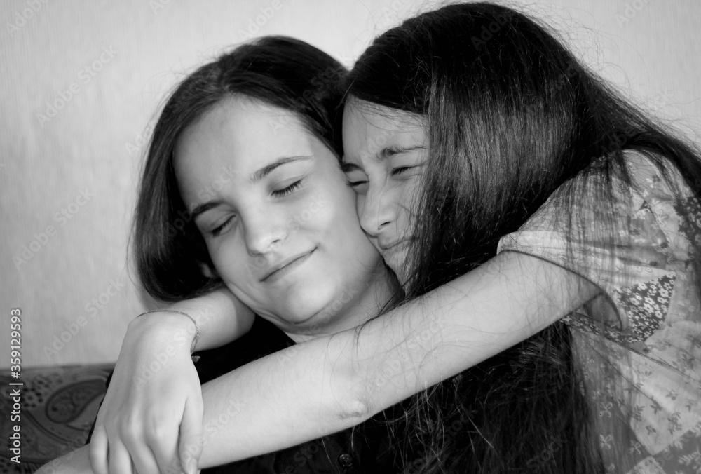 Fototapeta premium Black-and-white Portrait of two siblings, where the younger sister hugs the older one.