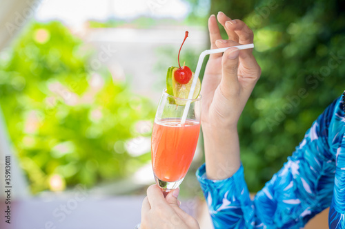 Asian woman relaxed on the beach with her red lime cherry cocktail in the hand in opening summer day