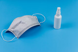 Protective disposable medical mask and hand sanitizer on blue background