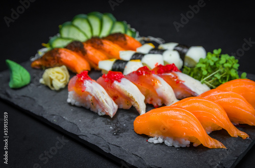 Sushi, traditional Japanese cuisine. Several delicious sushi on the decorated plate, black background. Group of sushi, Urakami, Nigori, Sushi jow, sashimi, tekamaki, etc ...