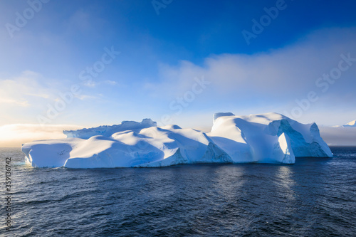 Huge floating non tabular iceberg, in its entirety, lit by golden evening light, with clearing mist, adventure cruise in the Bransfield Strait, near the Antarctic Peninsula, Polar Regions, Antarctica photo