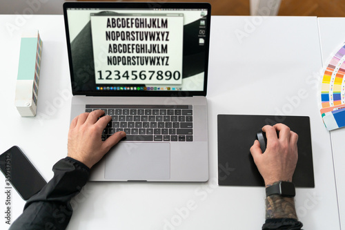 Close-up of male hands using laptop at office with alphabet on screen, man's hands typing on laptop keyboard in interior. Side view of businessman using computer