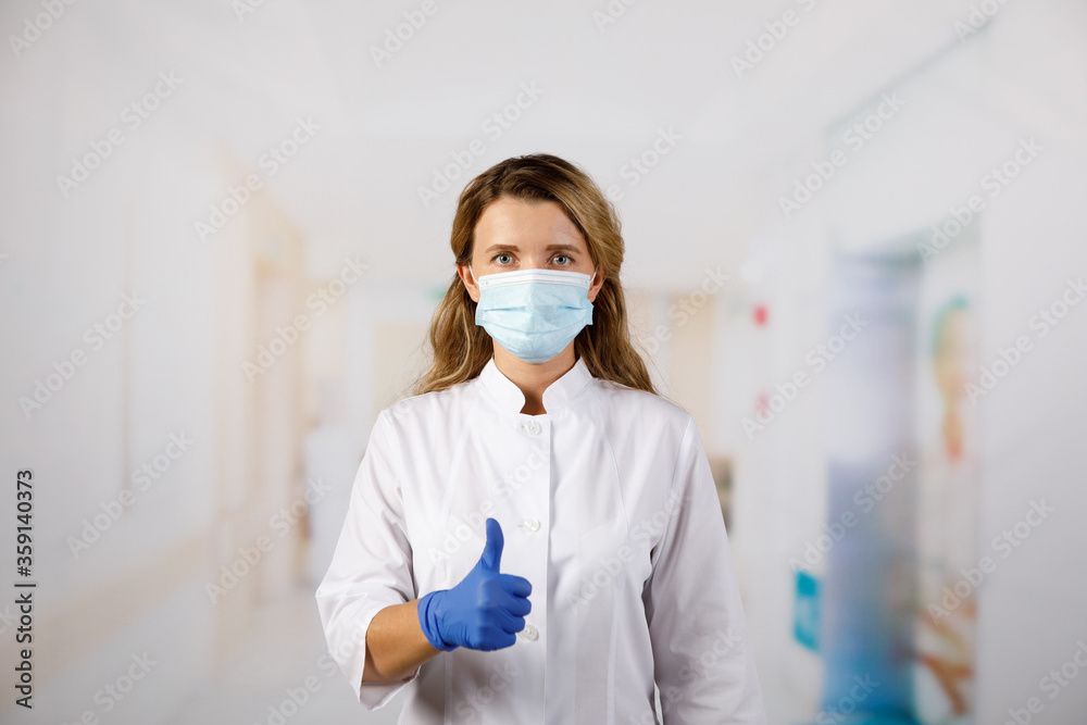 Φωτογραφία A woman in medical gloves and a face mask shows her fingers to the top and says