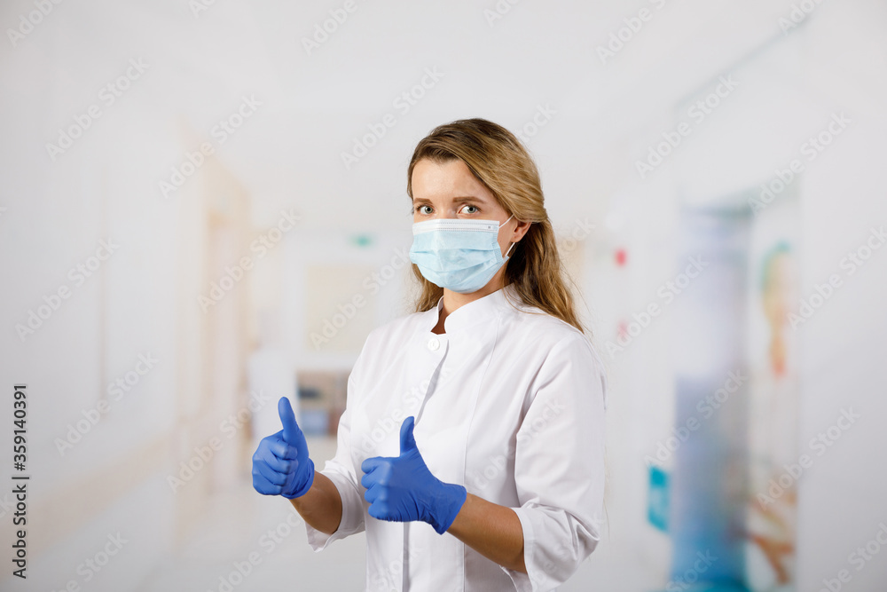 Φωτογραφία A woman in medical gloves and a face mask shows her fingers to the top and says