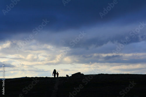 silhouette of man and kid hiking under dramatic sky