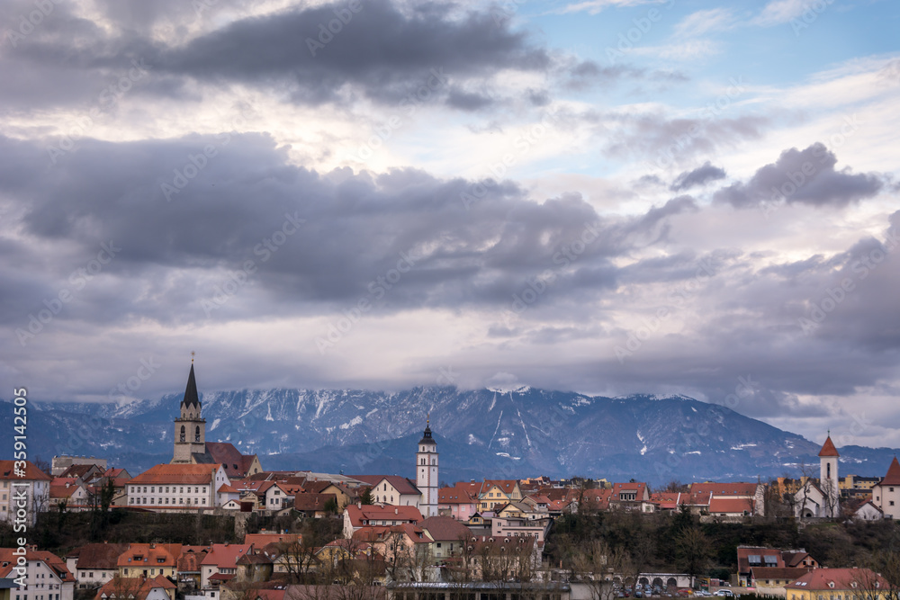 Panoramic view of medieval small town Kranj with Alps mountains covered with snow in the distance, Slovenia. Cloudy sky in winter season. Old churches with towers