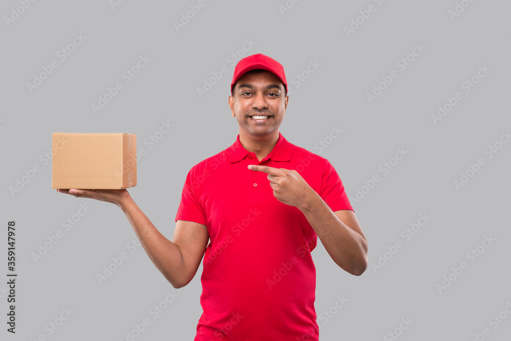 Delivery Man Pointing at Box in Hands Isolated. Red Tshirt Indian Delivery Boy. Home Delivery. Quarantine Hero.