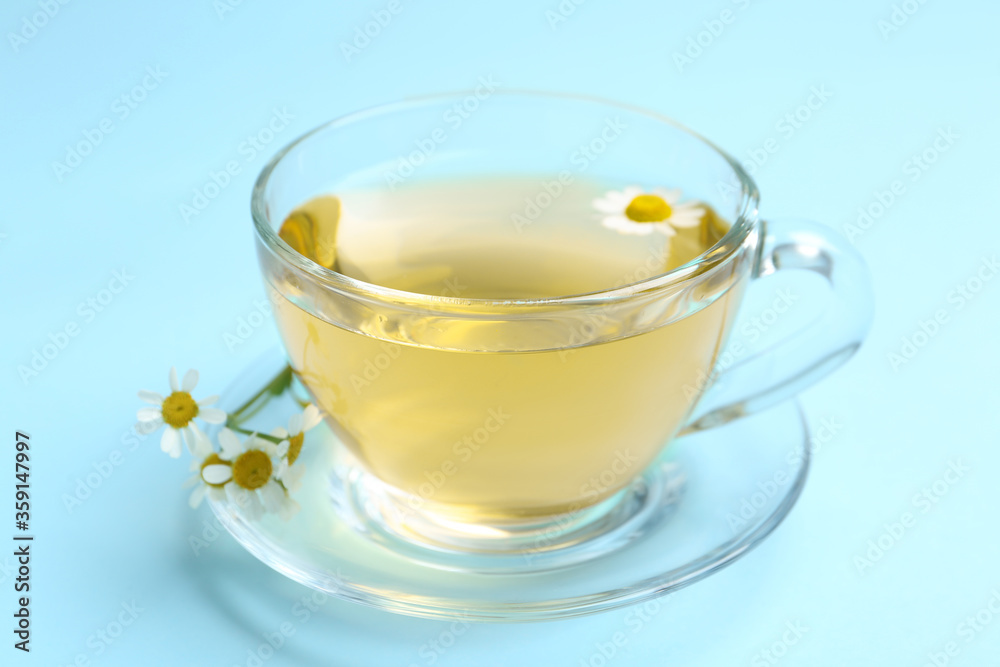 Delicious chamomile tea in glass cup on light blue background