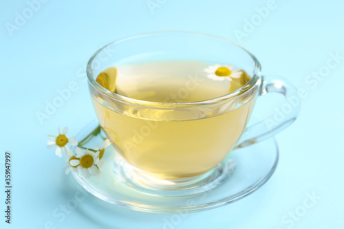 Delicious chamomile tea in glass cup on light blue background