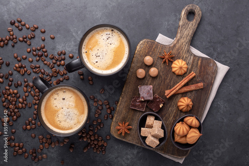 Coffee cups, coffee beans, various sweets and spice on stone background. Top view. Copy space