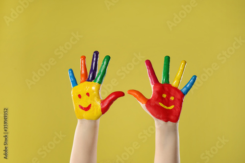 Kid with smiling faces drawn on palms against yellow background, closeup