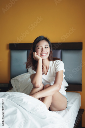 Young beautiful Asian woman sitting on bed at home. A woman smiling and relaxing. Woman lifestyle concept