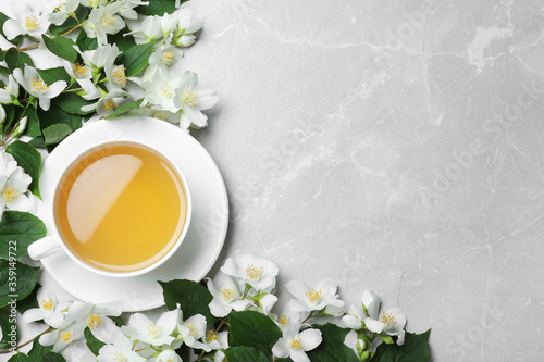 Cup of tea and fresh jasmine flowers on light grey marble table, flat lay. Space for text