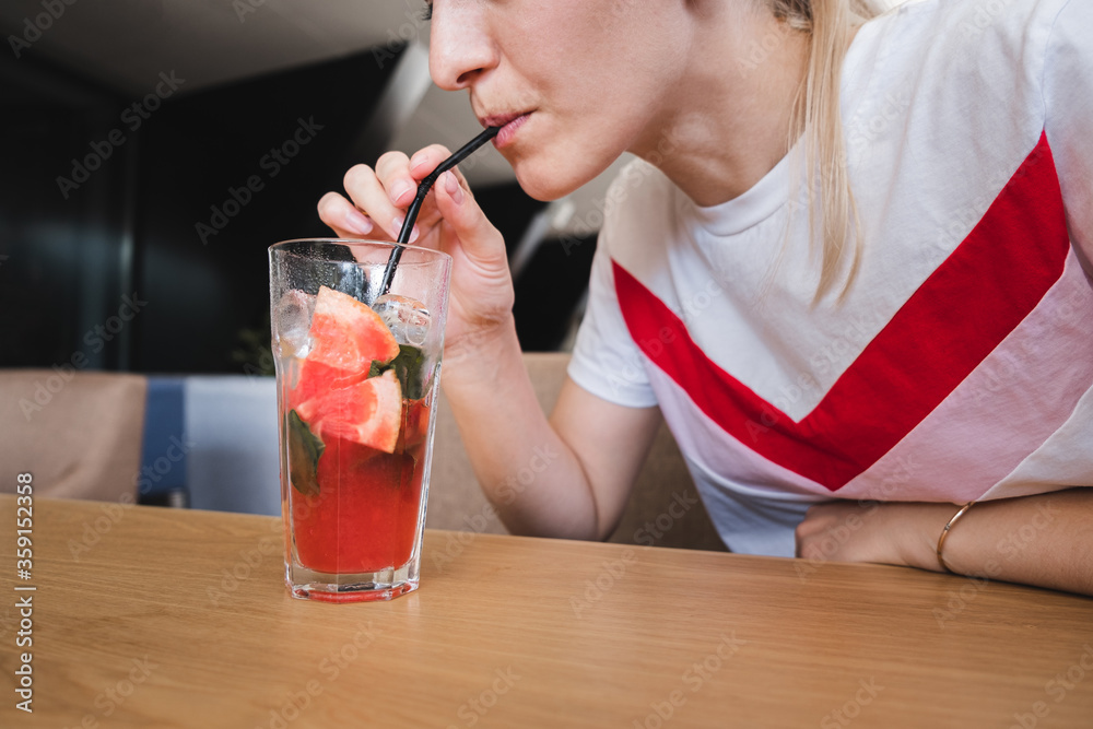 girl holds a glass and drinks a red drink with grapefruit, strawberries, mint and ice cubes through a straw. offline life. digital detox. girl holds a glass and drinks a red drink with grapefruit, strawberries, mint and ice cubes through a straw. offline life. digital detox.
