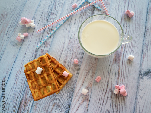 Breakfast for the child with milk, cookies and sweets. On a wooden surface is a cup of milk. Rectangular cookies, sweets and tubule for drinks on the table.