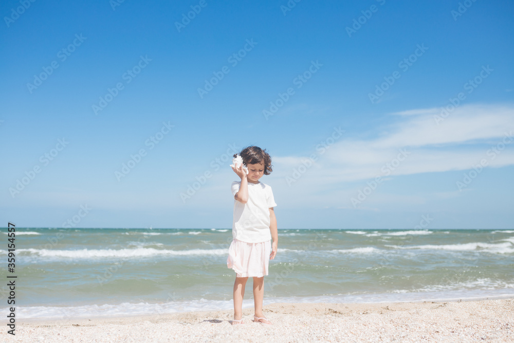 Little girl wearing light t-short and light pink skirt at the sea beach with a big beautiful seashell. Summer vacation Little girl wearing light t-short and light pink skirt at the sea beach with a big beautiful seashell. Summer vacation