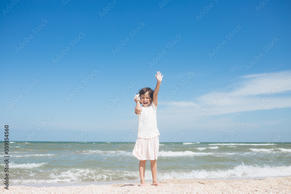 Little girl wearing light t-short and light pink skirt at the sea beach with a big beautiful seashell. Summer vacation Little girl wearing light t-short and light pink skirt at the sea beach with a big beautiful seashell. Summer vacation