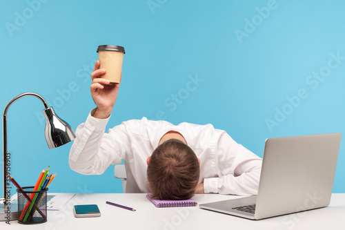 Exhausted male employee feeling fatigue lying on table and raising coffee cup, lack of energy in morning office, tired of stress problems sleeping at workplace, overwork concept. indoor studio shot photo