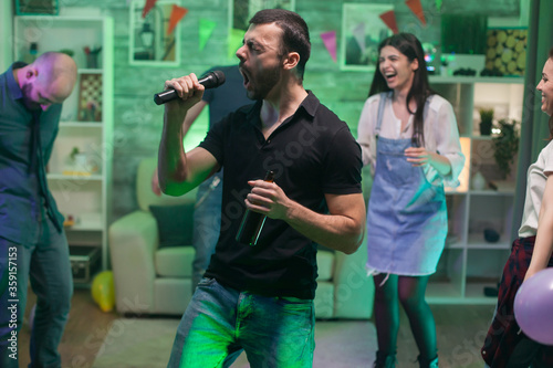 Bearded male singing a rock song on microphone while partying with his friends.