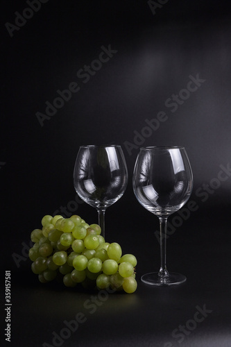 Still life on a black background. A glass wine glass and grape vine.