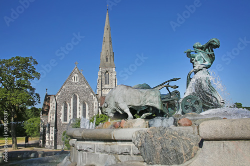 The Gefion Fountain with a group of animal figures being driven by the Norse goddess Gefjon on the harbour front with St Albans anglican church behind, Nordre Toldbod in Copenhagen, Denmark. photo