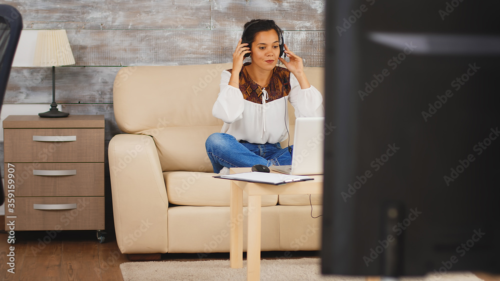 Woman using headphones during a video call while working from home sitting on couch in living room. Woman using headphones during a video call while working from home sitting on couch in living room.