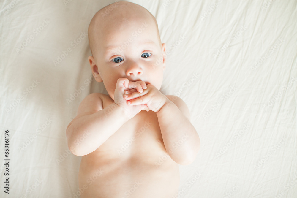 Cute baby lies on a white sheet and plays cheerfully, nibbles his hands Cute baby lies on a white sheet and plays cheerfully, nibbles his hands