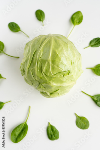 Fresh young green cabbage in the center and leaves of spinach around it on a white table. Vegeterian food. Vertical. Close-up. Top view