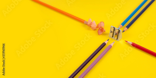 Some colored pencils of different colors and a pencil sharpener and pencil shavings on а yellow background