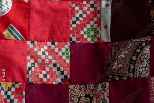 Red patchwork quilt fragment. Colorful handmade ethnic blanket. Worn clothes reuse concept.