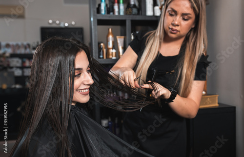 Female hairdresser makes hairstyle on young woman with brunette hair in salon.