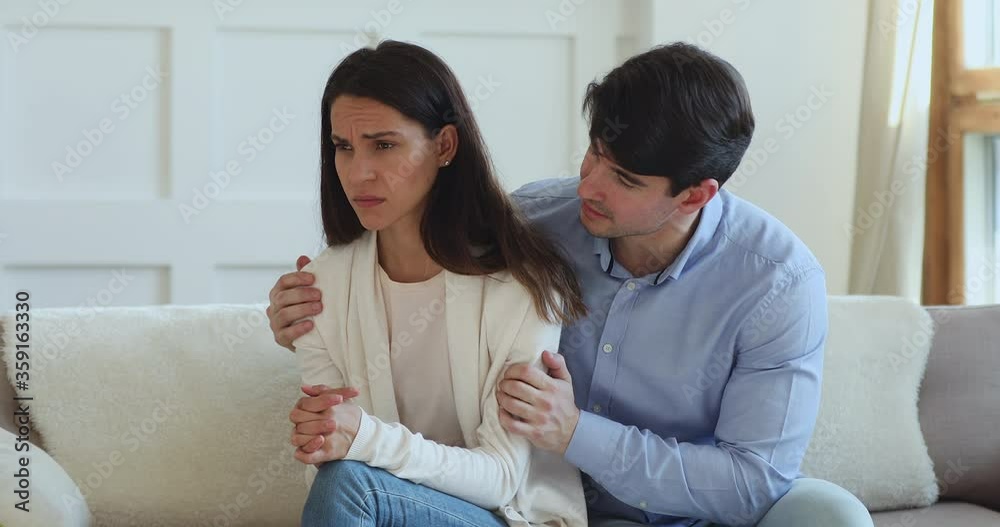 Young husband embracing offended stressed wife, apologizing for misunderstanding indoors. Worried millennial man feeling guilty, asking forgiveness, saying sorry to crying girlfriend, apology concept.