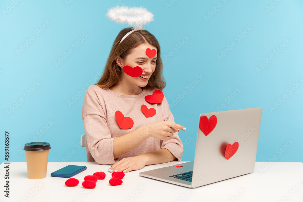 Hey you! Attractive angelic woman with kind expression sitting covered with sticker love hearts, pointing to laptop screen, indicating finger and choosing on video call. indoor studio shot, isolated Hey you! Attractive angelic woman with kind expression sitting covered with sticker love hearts, pointing to laptop screen, indicating finger and choosing on video call. indoor studio shot, isolated