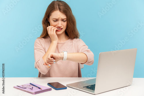 Fotografie Too late, no time to meet deadline! Upset worried woman employee sitting at workplace and looking at wrist watch with anxiety, nervous about late hour