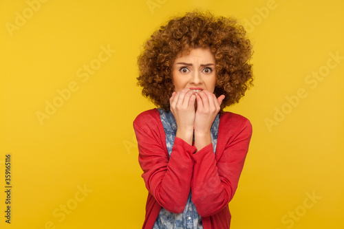 Depression, anxiety disorder. Portrait of stressed out, worried woman with curly hair biting nails and looking terrified, nervous about troubles. indoor studio shot isolated on yellow background