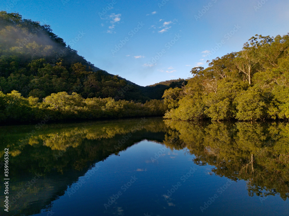 Beautiful morning view of Cockle creek with reflections of blue sky, foggy mountains and trees, Bobbin Head, Ku-ring-gai Chase National Park, New South Wales, Australia
