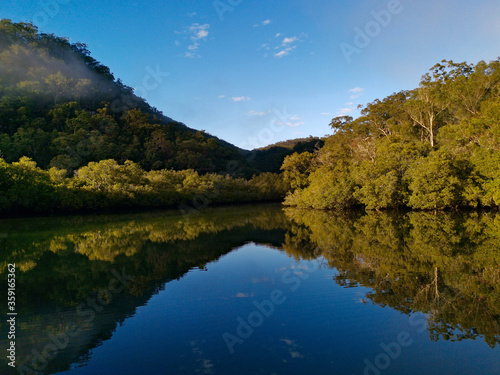 Beautiful morning view of Cockle creek with reflections of blue sky, foggy mountains and trees, Bobbin Head, Ku-ring-gai Chase National Park, New South Wales, Australia