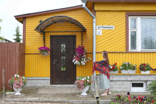 Russian woman in scarf. Folk style. Vintage wooden house in Suzdal town, Russia. Summer flowers in flowerpots in decoraive garden. Gardening. Flower decoration, decor photo