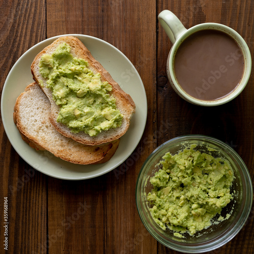 Tasty toasts with avocado and a cup of coffee for breakfast on plate on brown wooden table. Vertical. Top view