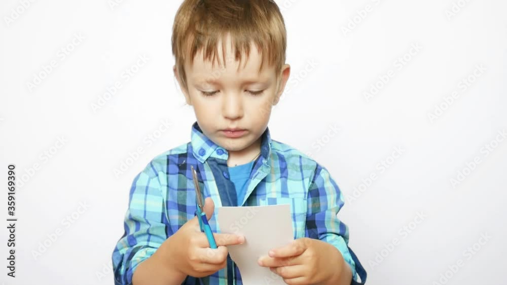 A beautiful little boy wearing blue plaid shirt cuts paper with scissors against white background A beautiful little boy wearing blue plaid shirt cuts paper with scissors against white background